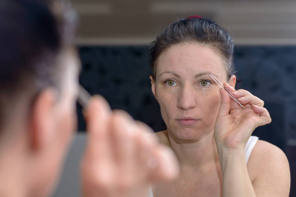 Жінка вириває брови пінцетом
 - Фото, зображення