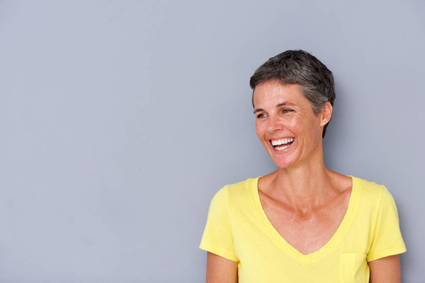 Portrait of beautiful middle age woman laughing by gray wall - Photo, Image