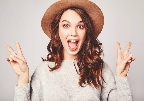 Portrait of young stylish laughing girl model in gray casual summer clothes in brown hat with natural makeup isolated on gray background. Looking at camera and showing peace sign - Fotografie, Obrázek