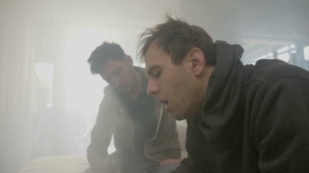 Young drug addicted boys consumers inhaling and exhaling smoke from a marijuana joint after sharing the cigarette inside the apartment - Filmmaterial, Video