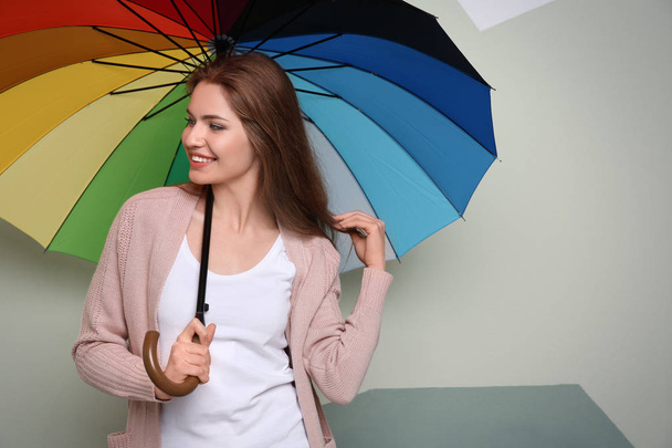Young woman with rainbow umbrella on color background - Foto, immagini