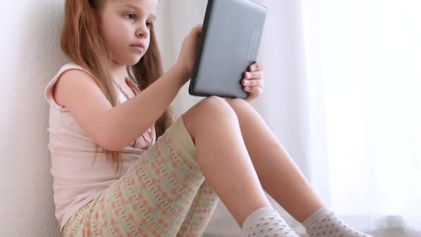 Baby little girl holding and using pc tablet and sits on the floor in room. - Video