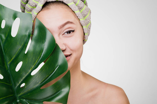 smiling young girl with clean skin holds a green leaf, on her head a towel, a day spa - Photo, image