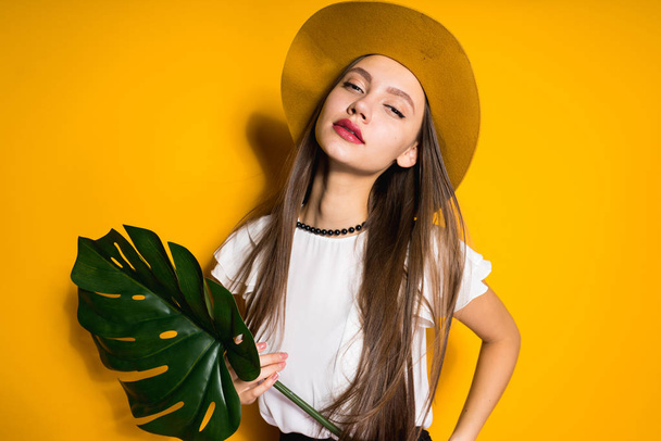 confident long-haired young girl model in a fashionable hat posing on a yellow background - Fotografie, Obrázek