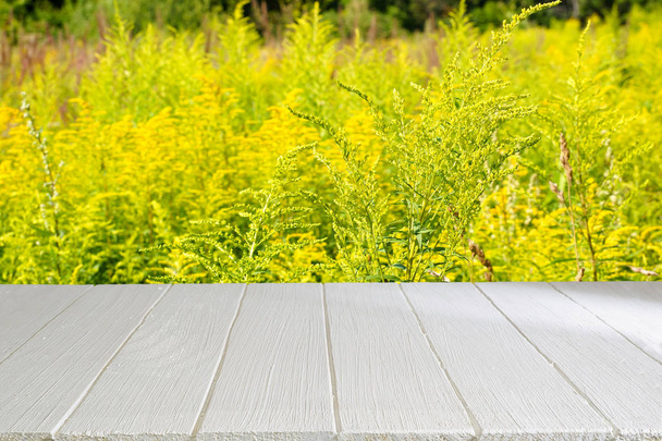 フィールドの草の背景に木製の白テーブル。空のテーブルは、あなたの製品を広告するため。わずかにぼやけて背景. - 写真・画像