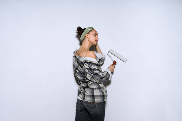 young girl painter in a plaid shirt colors the wall with a platen in white, repair in a new apartment - Foto, imagen