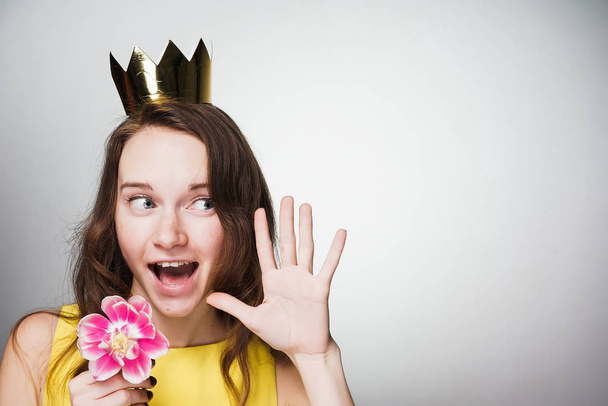 szczęśliwy zaskoczony młoda kobieta trzyma różowy kwiat w dłoniach, ma złotą koronę na głowie, z okazji dnia kobiet świata - Zdjęcie, obraz