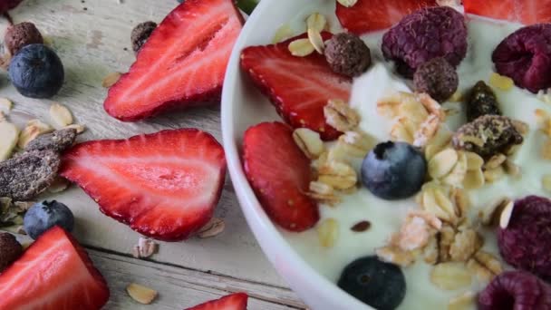 Gezond ontbijt, granen met yoghurt, aardbeien, bosbessen, frambozen en muesli op houten rustieke achtergrond. Begrip: fitness, voeding, wellness en ontbijt - Video
