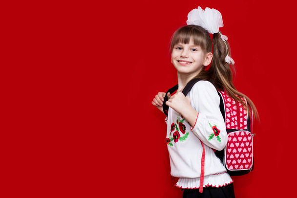 かわいい smilng 赤の背景にバックパックで学校制服と白い弓の小さな女の子。学校に戻る教育と学校のコンセプト - 写真・画像