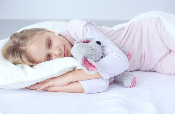 Child little girl sleeps in the bed with a toy teddy bear - Foto, immagini