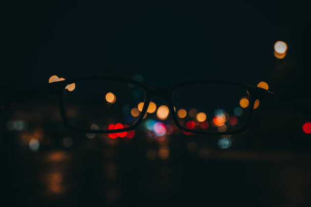 Paysage urbain nocturne avec gratte-ciel et lumières de la ville à travers une paire de lunettes. Image floue
. - Photo, image