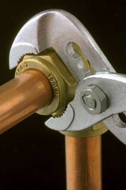 Chave ajustável do encanador que aperta acima a tubulação de cobre Uma chave ajustável que aperta acima de um cotovelo da compressão a tubulação de cobre de 15mm em um fundo preto
 - Foto, Imagem