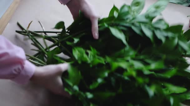 Florist puts greens on an empty sheet of kraft paper for the arrangement of a bouquet - Πλάνα, βίντεο