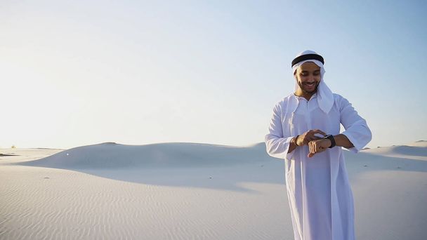 Nowoczesny mężczyzna sheikh wykorzystuje inteligentny zegarek i stoi w środku bott - Zdjęcie, obraz
