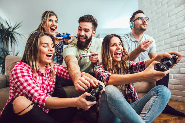Grupo de amigos juegan videojuegos juntos en casa, divirtiéndose. - Foto, Imagen