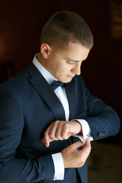 Een zelfverzekerde elegante knappe jonge man knoppen Manchetknopen. - Foto, afbeelding