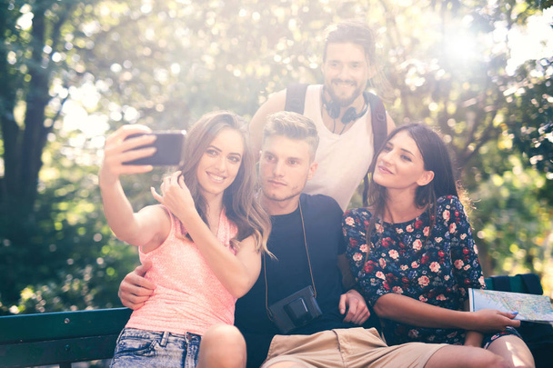 Skupina čtyř a utekli s selfie s chytrý telefon v letním parku - Fotografie, Obrázek