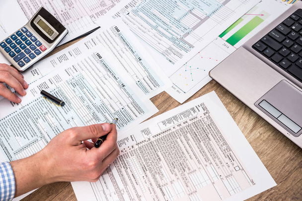 Empresario llenando formulario de impuestos 1040 con ayuda portátil en el escritorio de la oficina
 - Foto, imagen