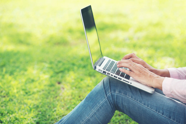 Jeune belle femme travaillant en plein air dans un parc public. Travailler sur ordinateur portable à l'extérieur. Image recadrée d'une femme travaillant sur un ordinateur portable assis dans un parc
. - Photo, image