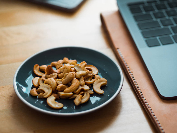 Some cashew nuts on small snack dish on work desk. - Фото, изображение