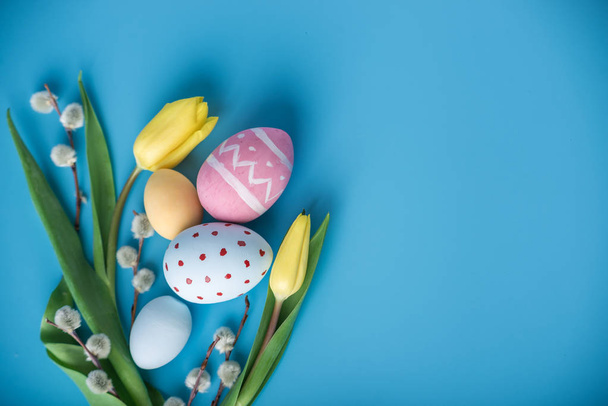Színes húsvéti tojás sárga tulipán kézzel festett kék háttérrel. Tavaszi üdvözlőlap-ünnep - Fotó, kép