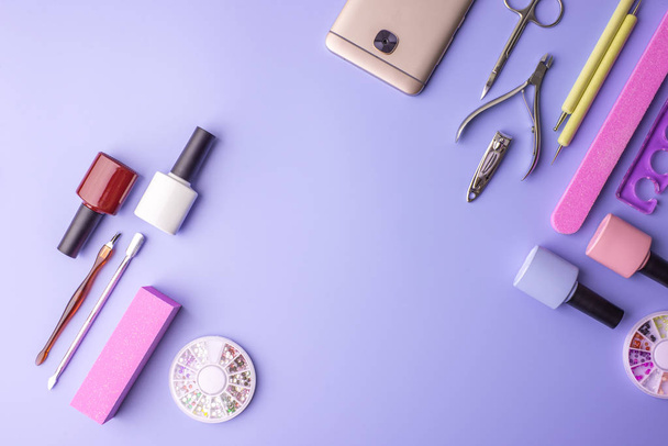 Ensemble d'outils cosmétiques pour manucure et pédicure sur fond violet. Polis à gel, limes à ongles et tondeuses, vue de dessus
 - Photo, image