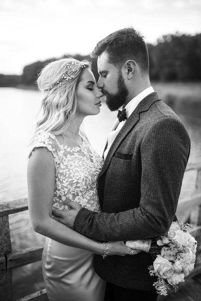 Stylish couple of happy newlyweds posing in the park on their wedding day. Perfect couple bride, groom posing and kissing  - Fotó, kép