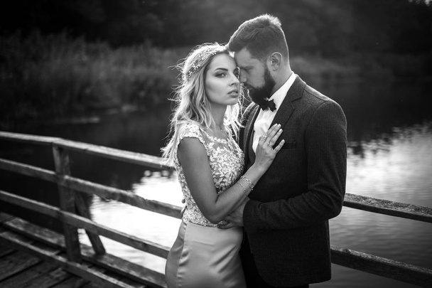 Stylish couple of happy newlyweds posing in the park on their wedding day. Perfect couple bride, groom posing and kissing  - Fotó, kép