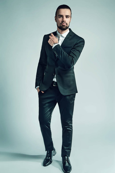 portrait of handsome fashion stylish hipster lumbersexual businessman model dressed in elegant black suit posing on studio background. Metrosexual - Photo, image