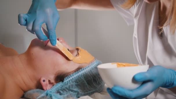 Detail osoby, která navštívit kosmetický salon, ovocné maska se aplikuje na obličej s speciální dřevěnou tyčí - Záběry, video