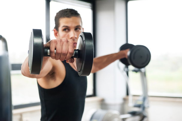 Young man exercising with dumbbells in a gym, focus on the weight - Fotografie, Obrázek