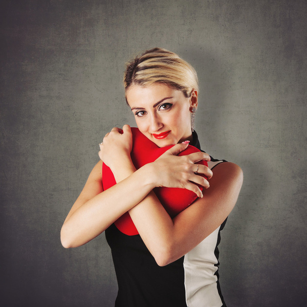 Attractive blonde woman portrait holding red heart against grunge background - Foto, Imagem
