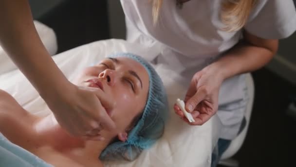 Cosmetologist εφαρμογή κρέμας στο πρόσωπο στους πελάτες μετά την καλλυντική διαδικασία - Πλάνα, βίντεο
