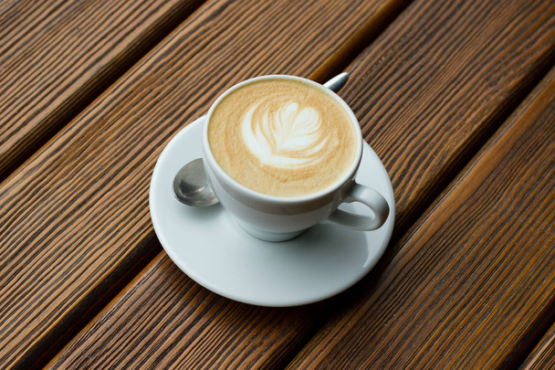 Cappuccino in weißer Tasse mit Löffel auf Holztisch  - Foto, Bild