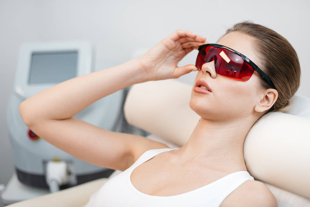 The side portrait of the young attractive woman with natural make-up wearing the safety goggles while lying in beauty salon. - Photo, image
