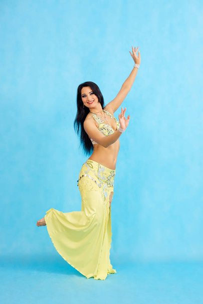Charming dancer performs oriental belly dance on a blue background. - Φωτογραφία, εικόνα