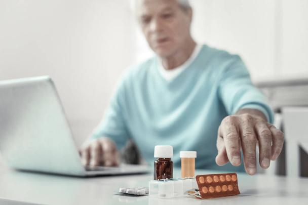 Aged senior man sitting and holding hand near pills. - Фото, зображення