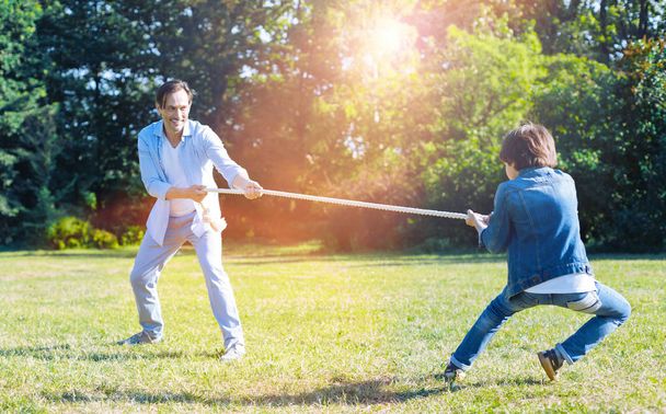 Excited father and son playing tug of war together - 写真・画像