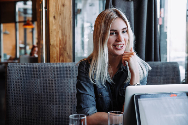 a beautiful blonde businesswoman in a denim shirt sits in a restaurant and communicates with her friends - 写真・画像