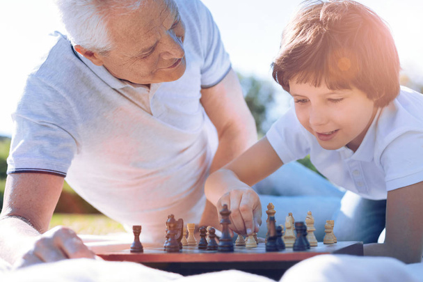 Thoughtful granddad watching smart grandchild playing chess - Zdjęcie, obraz