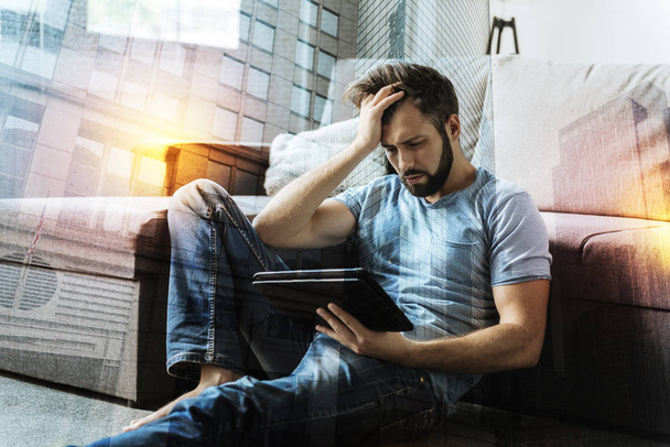 Emotional person frowning while sitting on the floor with his tablet - Foto, afbeelding