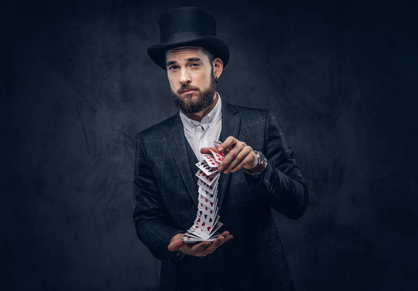 Portret van een knappe goochelaar in een zwart pak, truc met speelkaarten tonen op een donkere achtergrond. - Foto, afbeelding