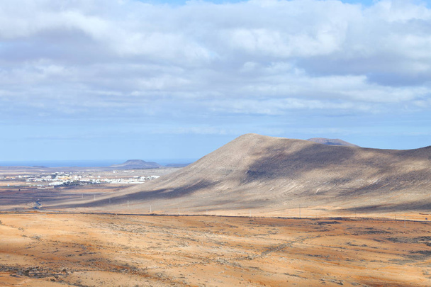 Aerial view of arid desert valley with volcano peaks, coast village, on a summer, cloudy day, Fuerteventura, Canary Islands, Spain . - Fotoğraf, Görsel