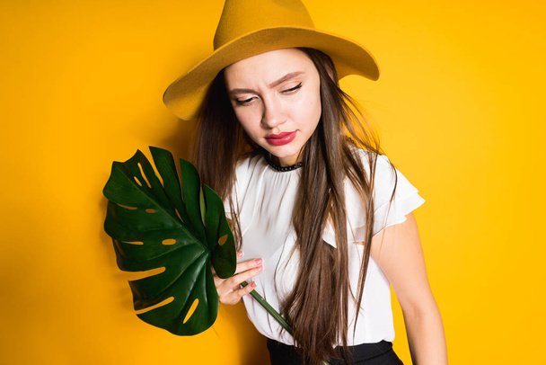 pensive woman in a hat holds a green leaf in her hands - Foto, Bild