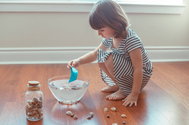 Portrait of cute white Caucasian preschooler girl playing with paper ships and water indoors at home. Early creativity  development, children activity. Dreams of adventure travel concept - Photo, Image