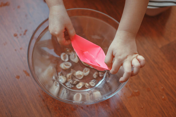 macro close-up de mãos de crianças brincando com navios de papel e água dentro de casa. Desenvolvimento de criatividade precoce, atividade de crianças. Sonhos de aventura, conceito de viagem
 - Foto, Imagem