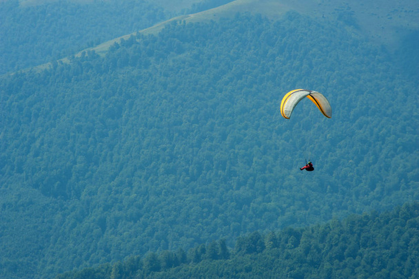 El parapente vuela sobre un valle montañoso en un soleado día de verano. Parapente en los Cárpatos en el verano
.  - Foto, Imagen