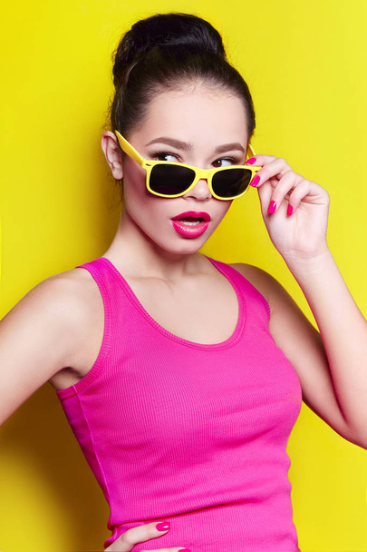 Beautiful cheerful cheerful young girl in sunglasses wearing yellow glasses on a yellow background laughing.  - Zdjęcie, obraz