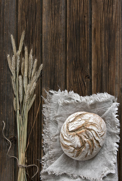 top view of homemade baked traditional bread on grey scarf with wheat on wooden background - Fotó, kép