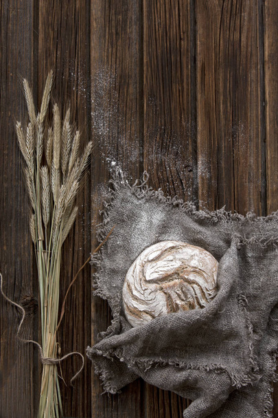 close-up of delicious homemade traditional bread with flour and wheat on wooden background - Fotó, kép